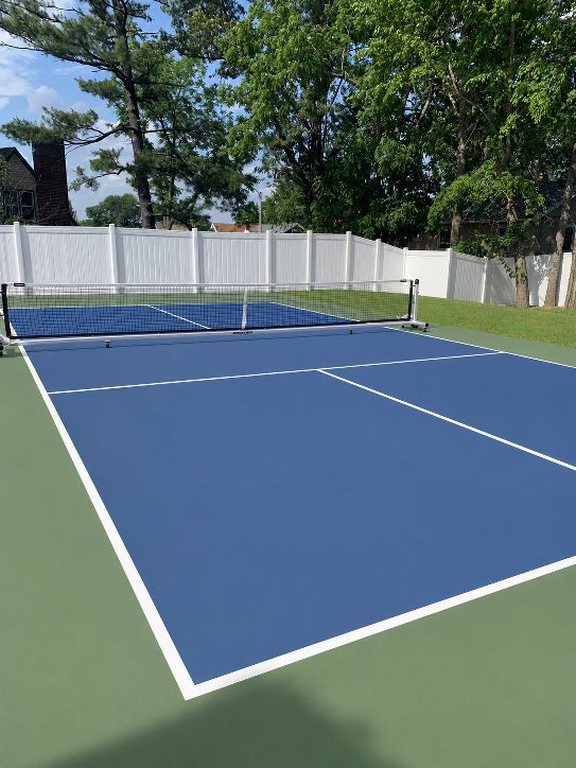 AI concept visualization generated from that photograph, adding a multi-use game court with black containment fencing inside the same vinyl fence line.