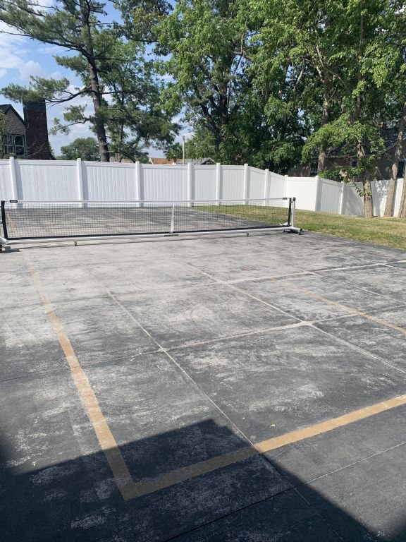 Client site photograph: worn lawn and an ageing slab behind a white vinyl privacy fence.
