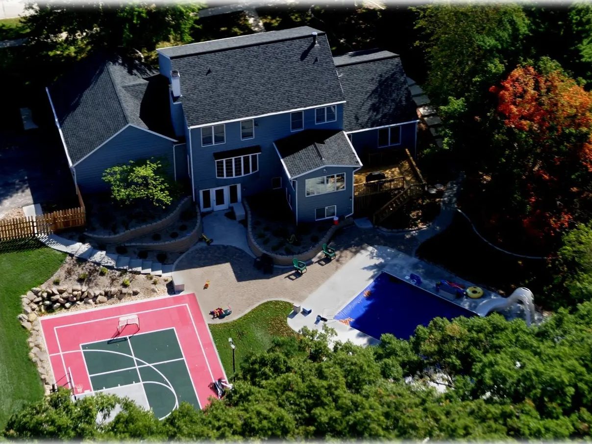 Aerial photograph of the same pool yard with the finished red and green multi-use game court in place beside the pool.