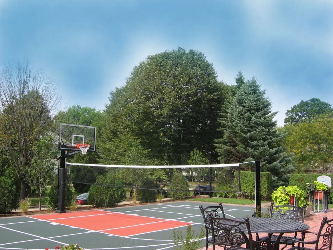 Eye-level photograph from the same patio showing the finished red and teal court surface, white lines, hoop and perimeter posts.