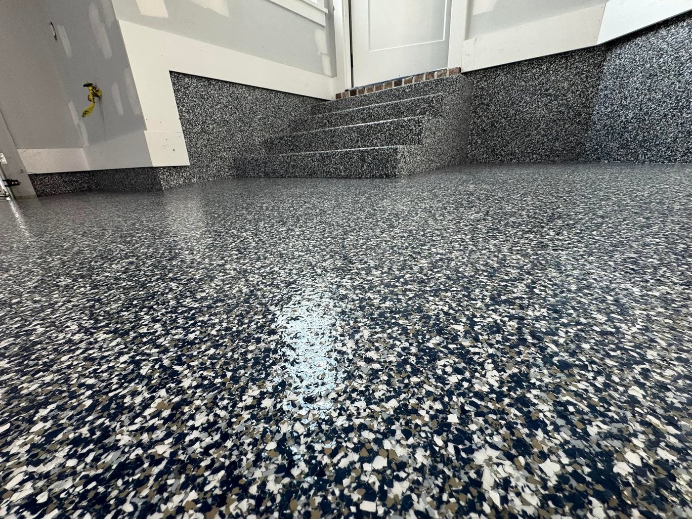 Finished navy, grey and white flake epoxy floor in a residential garage, with the same flake coating carried up a short flight of steps, the cove base and the lower walls.