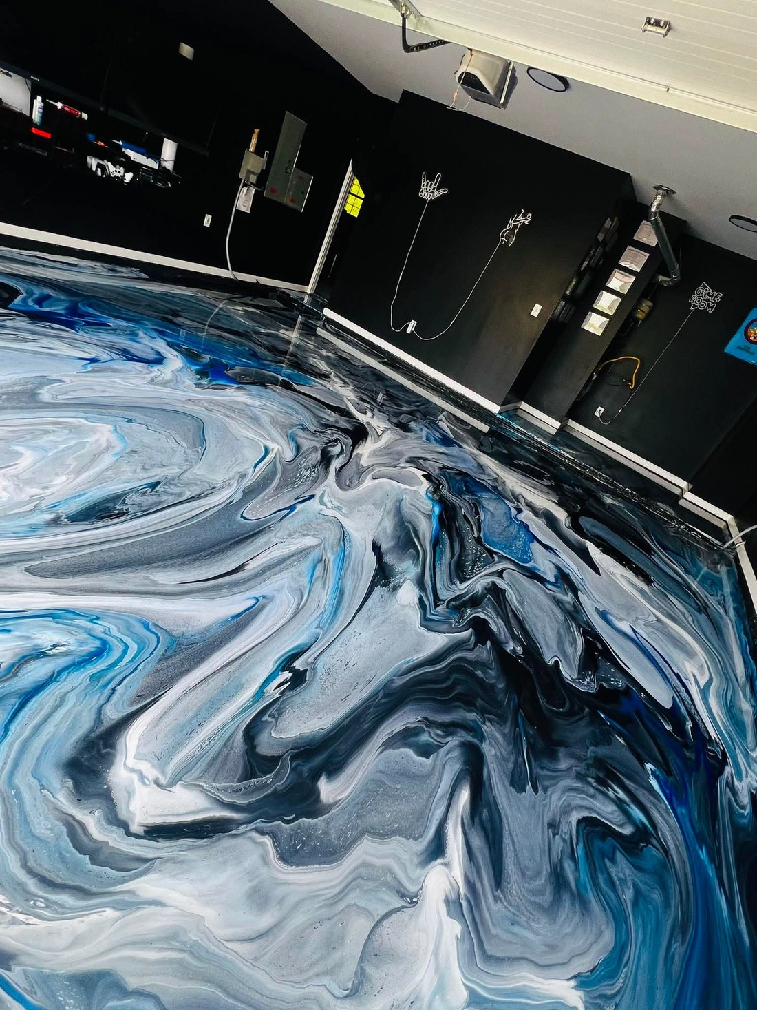 Finished blue and white metallic epoxy floor with a swirled marbled pattern in a workshop with black walls and mounted tools.